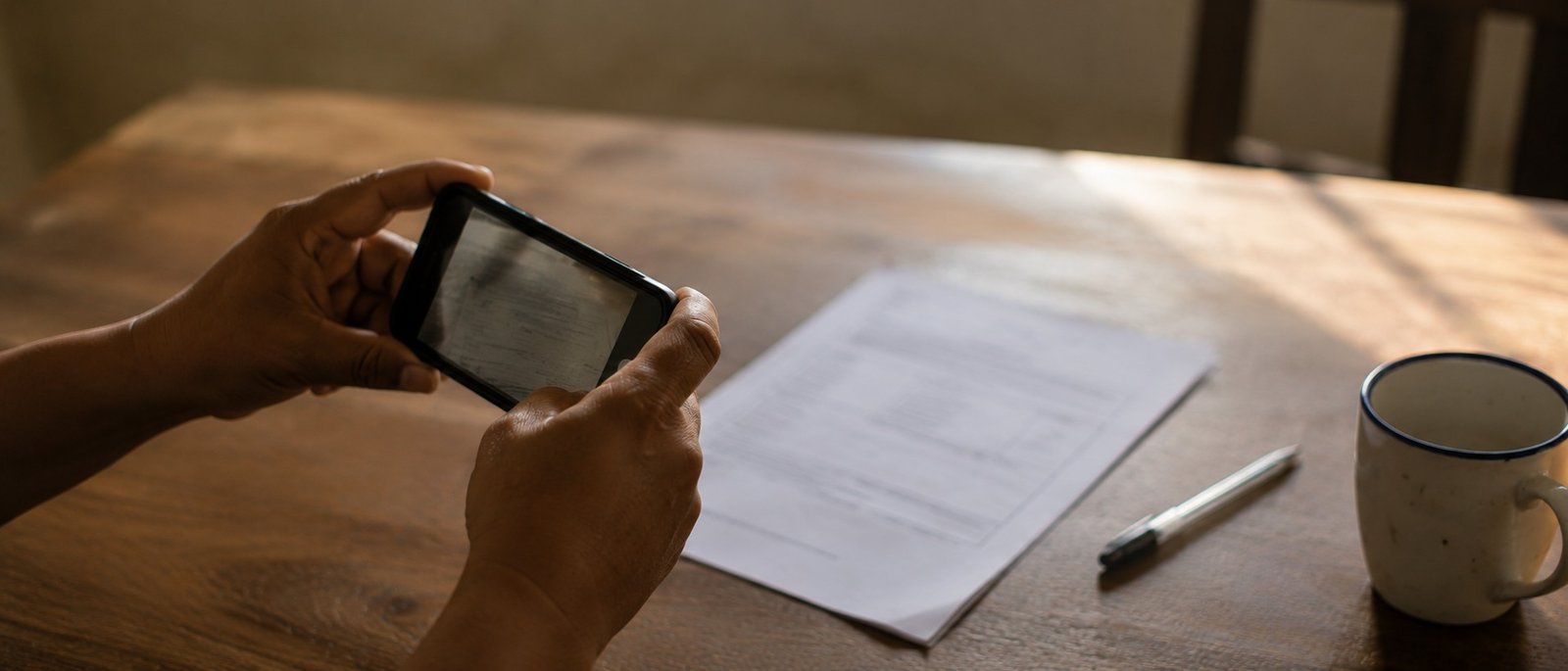 Mãos fotografando um documento com o celular sobre a mesa de casa, atendimento jurídico a distância por WhatsApp
